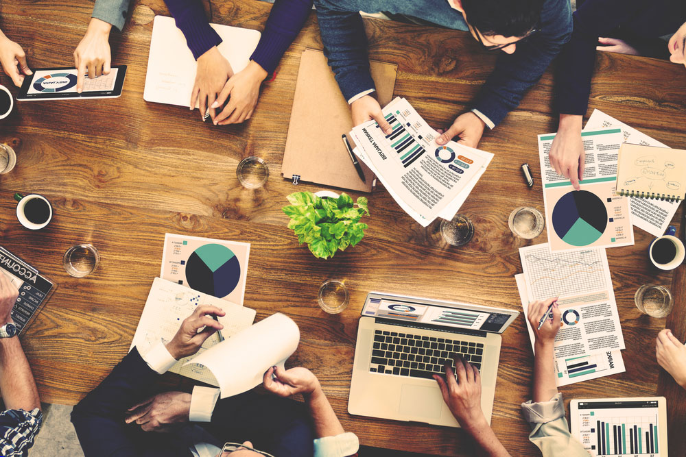 Overhead view of marketing team at a conference table working on a project with laptops, coffee and pages with graphs and pie charts.